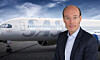 Mand i jakkesæt står foran et privatjet på en landingsbane under blå himmel.