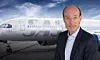 Mand i jakkesæt står foran et privatjet på en landingsbane under blå himmel.