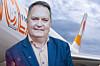 Man i kostym står framför ett Ving-flygplan mot molnig himmel.