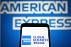 Smarttelefon som visar American Express Global Business Travel-logotyp framför American Express-skylt.