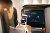 En person holder en smartphone foran en flyskærm med sædeunderholdning.