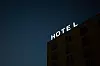 Upplyst hotellskylt på en byggnad mot mörk blå kvällshimmel.