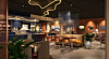 Digital rendering av en hotellobby med bar, soffor, bord och växter i varm belysning.