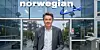 En mand står foran en glasfacade med Norwegian-logo og et flysymbol ved indgangen.