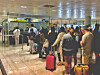 Mennesker i kø med kufferter foran check-in skranker i en lufthavnsterminal.