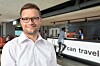 En mand i hvid skjorte står foran en receptionsdisk i et hostel med skiltet 'can travel' i baggrunden.