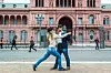 Två personer dansar på en stenlagd gata framför en rosa byggnad med valv, fönster och balkonger.