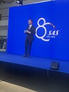 En mand står på en blå scene foran et stort SAS-logo og tallet 80.
