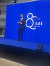 En mand står på en blå scene foran et stort SAS-logo og tallet 80.