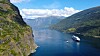Två fartyg seglar i en smal fjord i Flåm i Norge mellan höga berg och grönklädda sluttningar.
