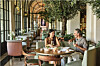 Elegant hotel restaurant with arched windows, upholstered chairs and guests dining in Florence.