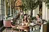 Elegant hotel restaurant with arched windows, upholstered chairs and guests dining in Florence.