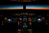 Flygplanscockpit med upplysta instrument och mörk himmel med färgad horisont utanför framrutan.