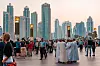 Folksamling på en promenad framför Dubais höga skyskrapor i kvällsljus.